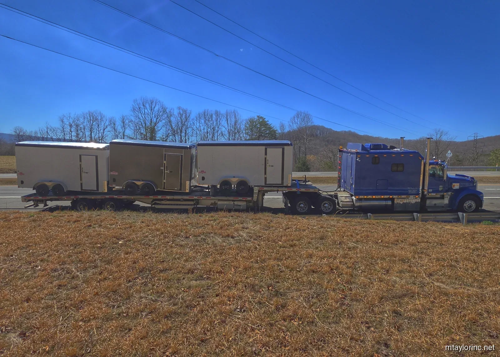 M Taylor Inc stepdeck stacked with three enclosed cargo trailers on mountain highway